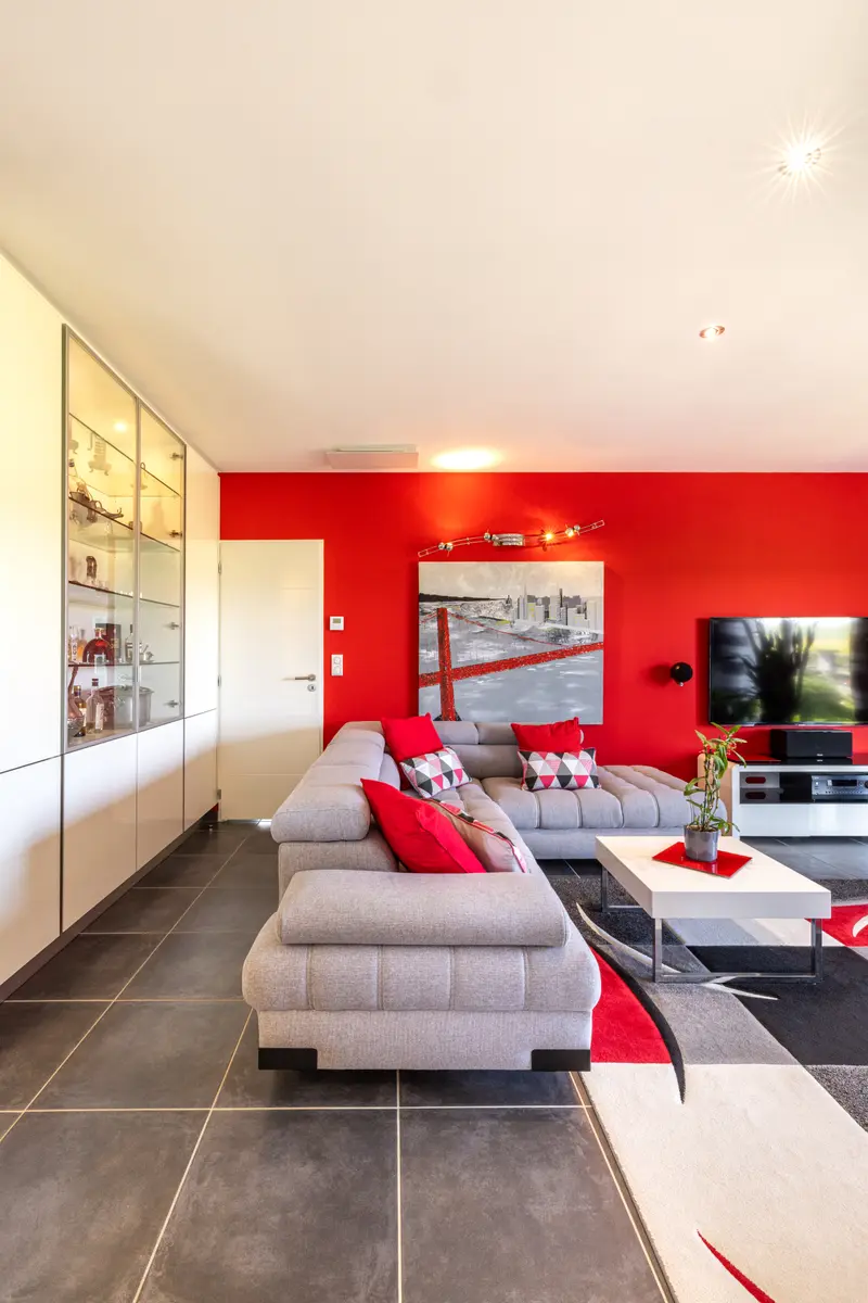 Le salon, canapé d’angle gris et mur rouge
