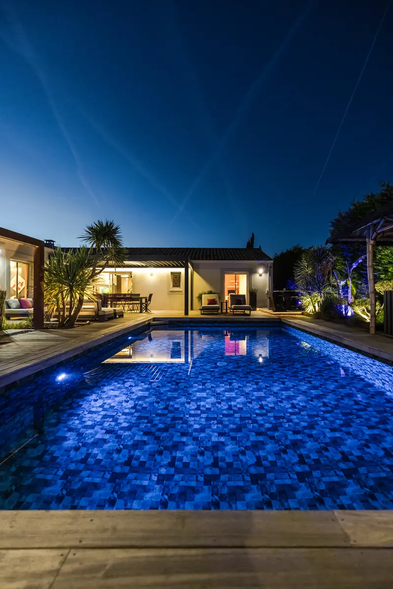 La piscine éclairée et la façade à la nuit tombée